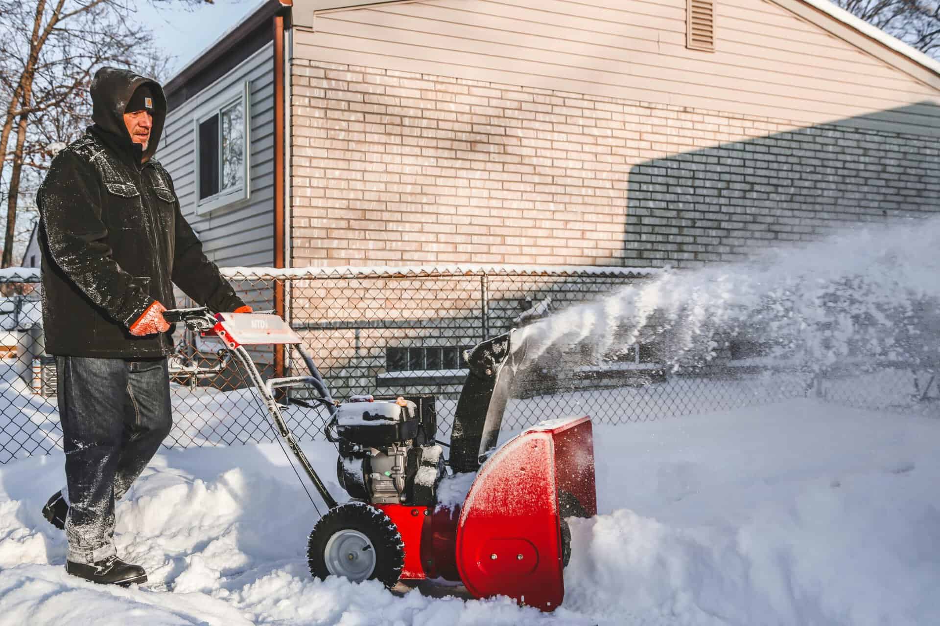 Man using snowblower clearing driveway and walkway for winter maintenance.